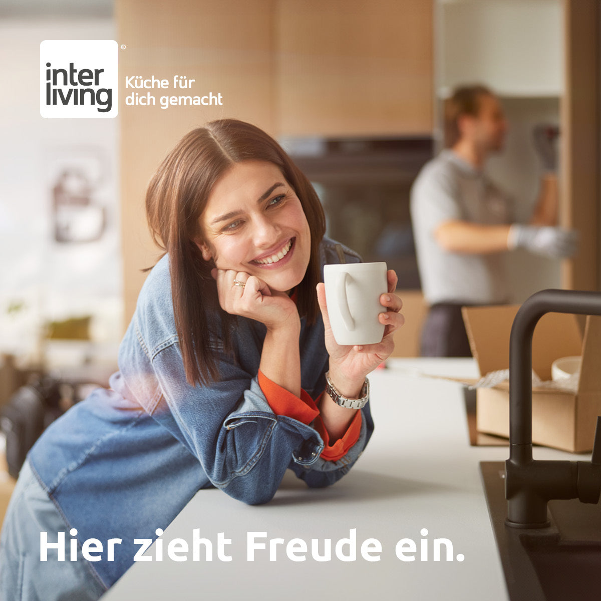 Frau genießt Kaffee an neuer Küchenarbeitsplatte, während im Hintergrund Umzugskartons ausgepackt werden – termingerechte Küchenlieferung von Interliving FREY