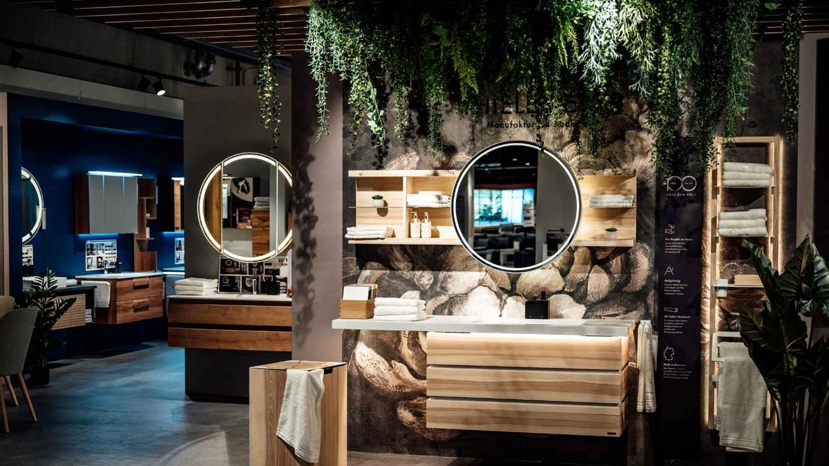 Badmöbel aus hellem Holz mit runden, beleuchteten Spiegeln und Pflanzendekoration in der Bad-Ausstellung von Interliving FREY