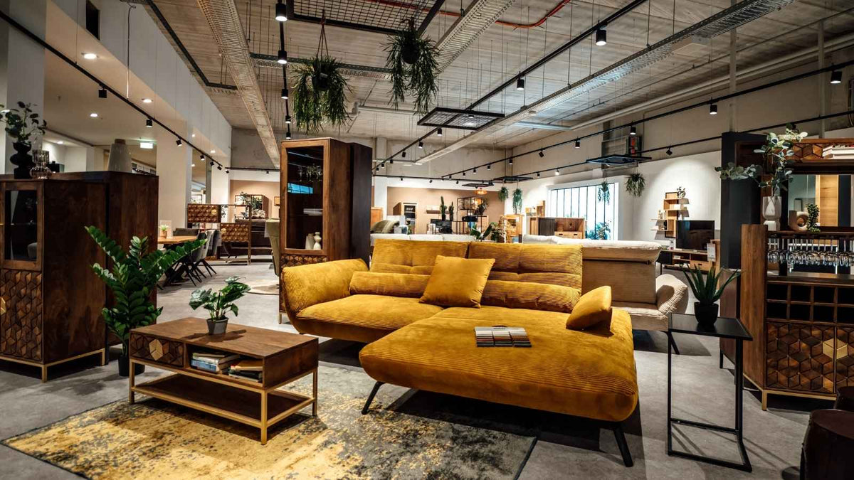 Senfgelbes Ecksofa aus Cord mit Couchtisch und Vitrinen aus dunklem Holz in der Wohnzimmer-Ausstellung von Interliving FREY