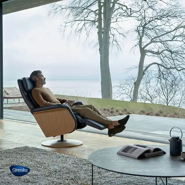 Stressless Relaxsessel mit Holzrückseite und Nutzer vor großer Fensterfront